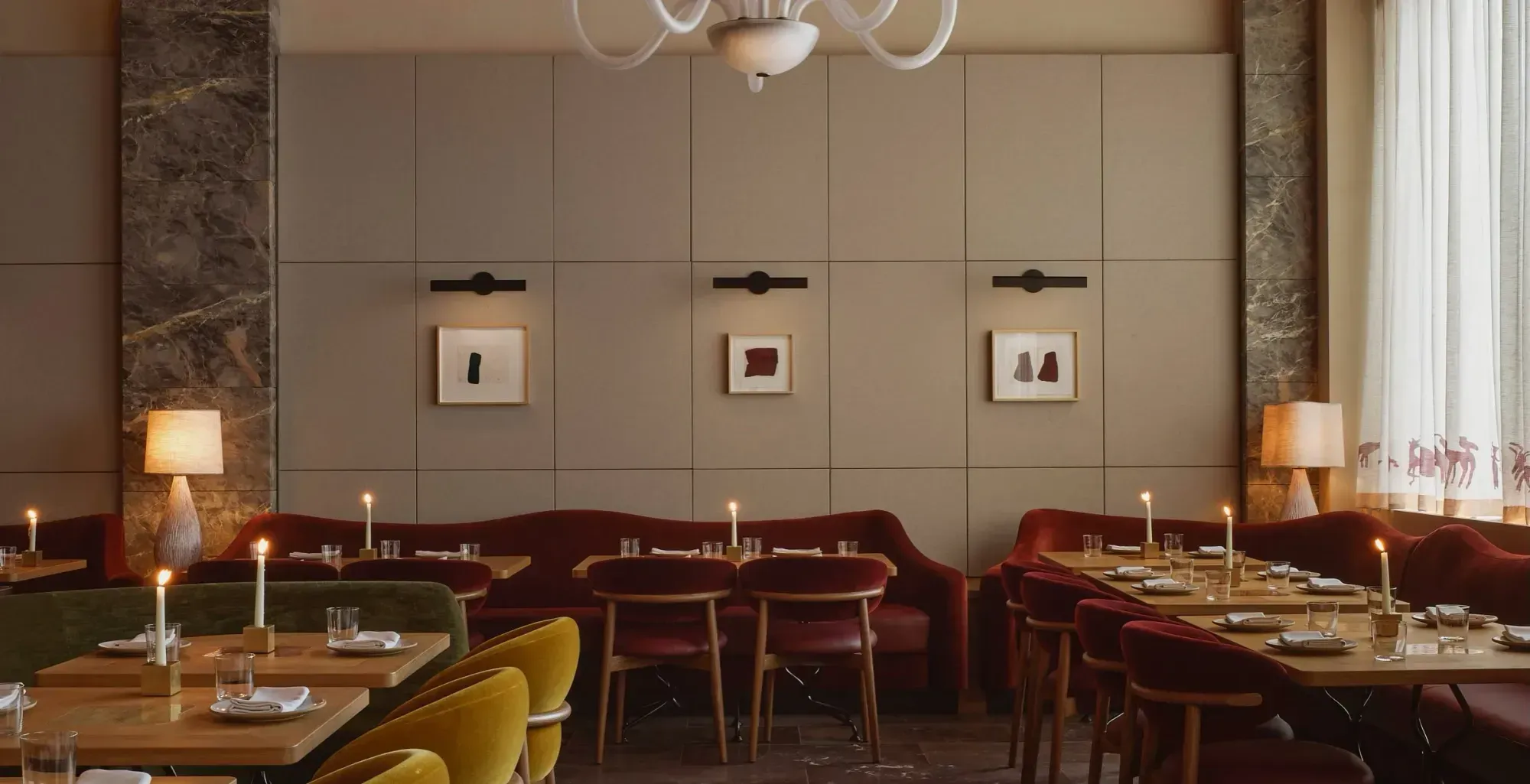 The dining room at Humm: set tables and mustard velvet chairs in front of a burgundy banquette, three small framed works on a pale panelled wall, and a white glass chandelier above