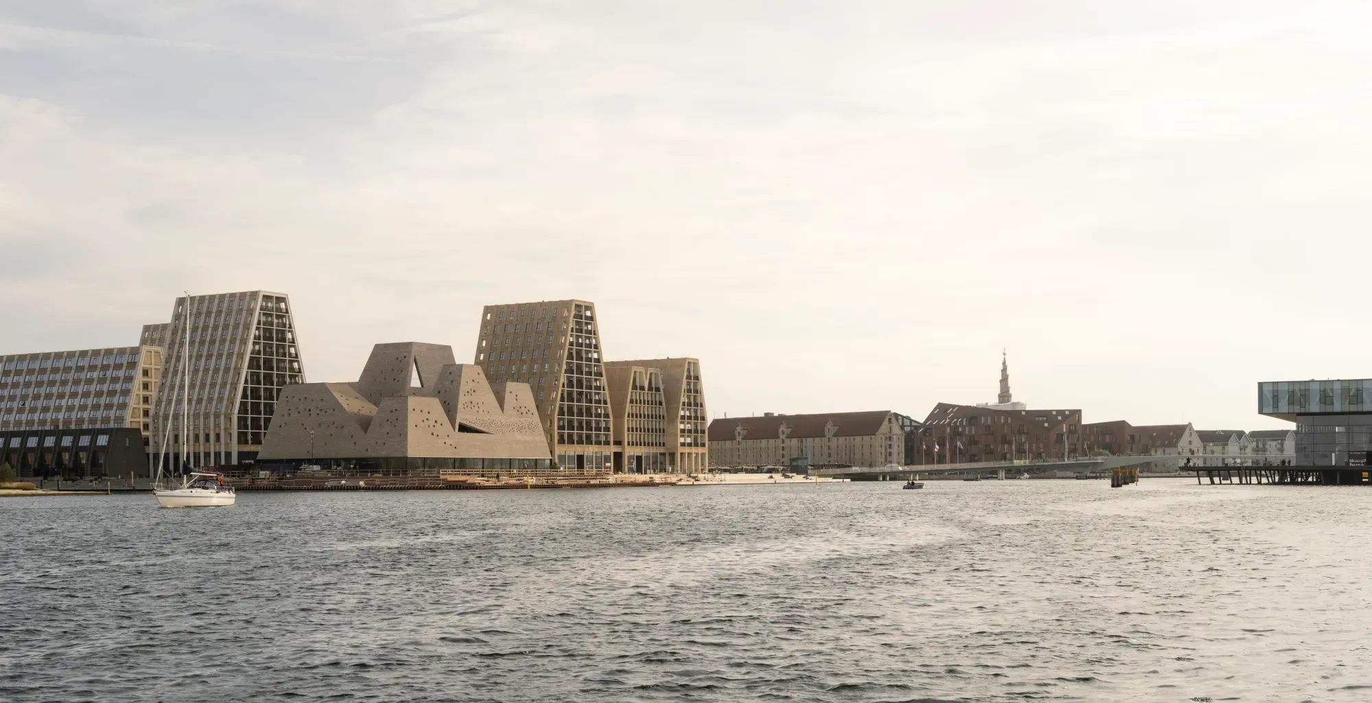 KAI's five brick towers on Papirøen seen across Copenhagen's Inner Harbour, with a sailboat in front