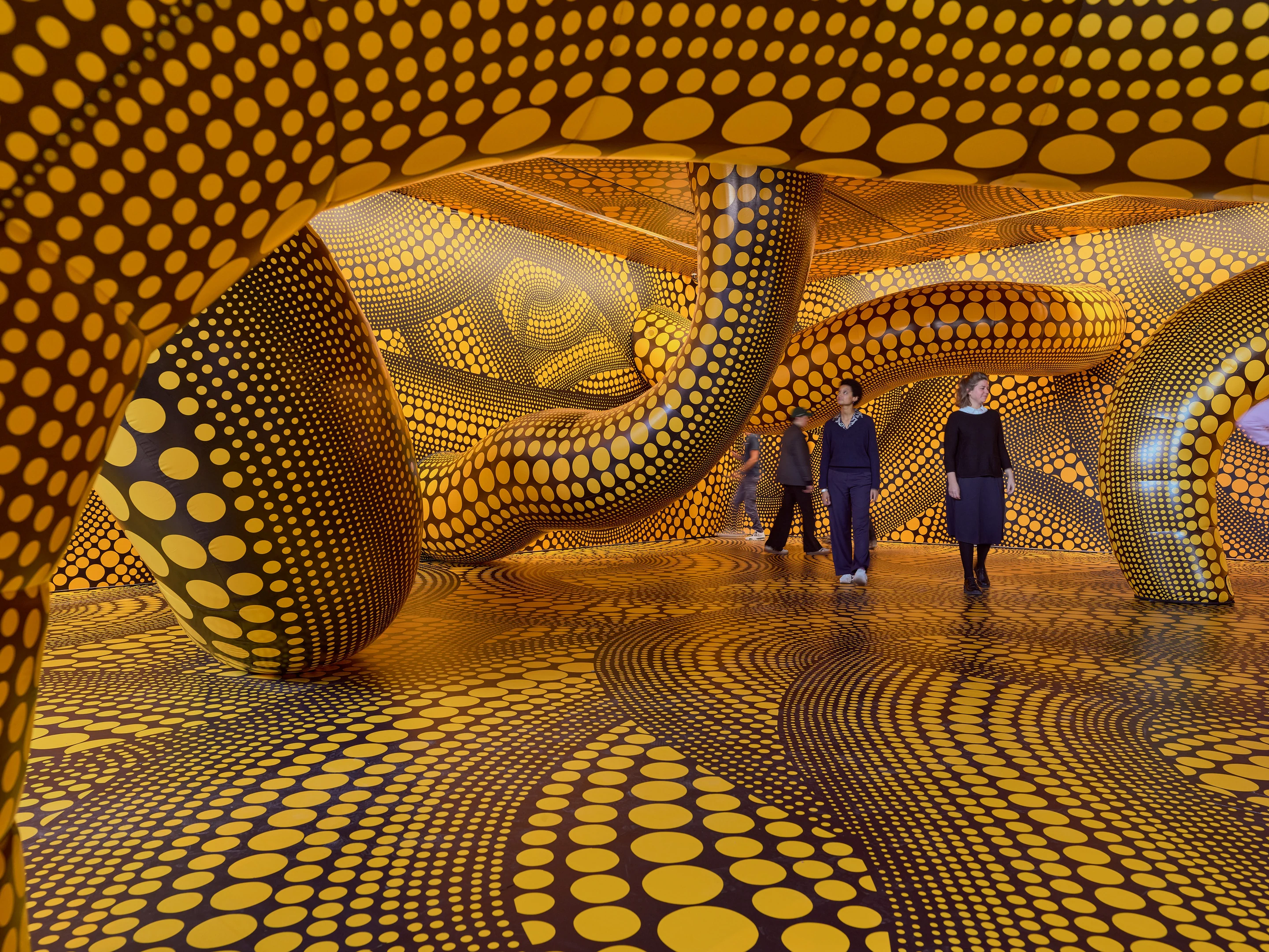 Room lined floor to ceiling with gold and black polka-dot forms, visitors walking through